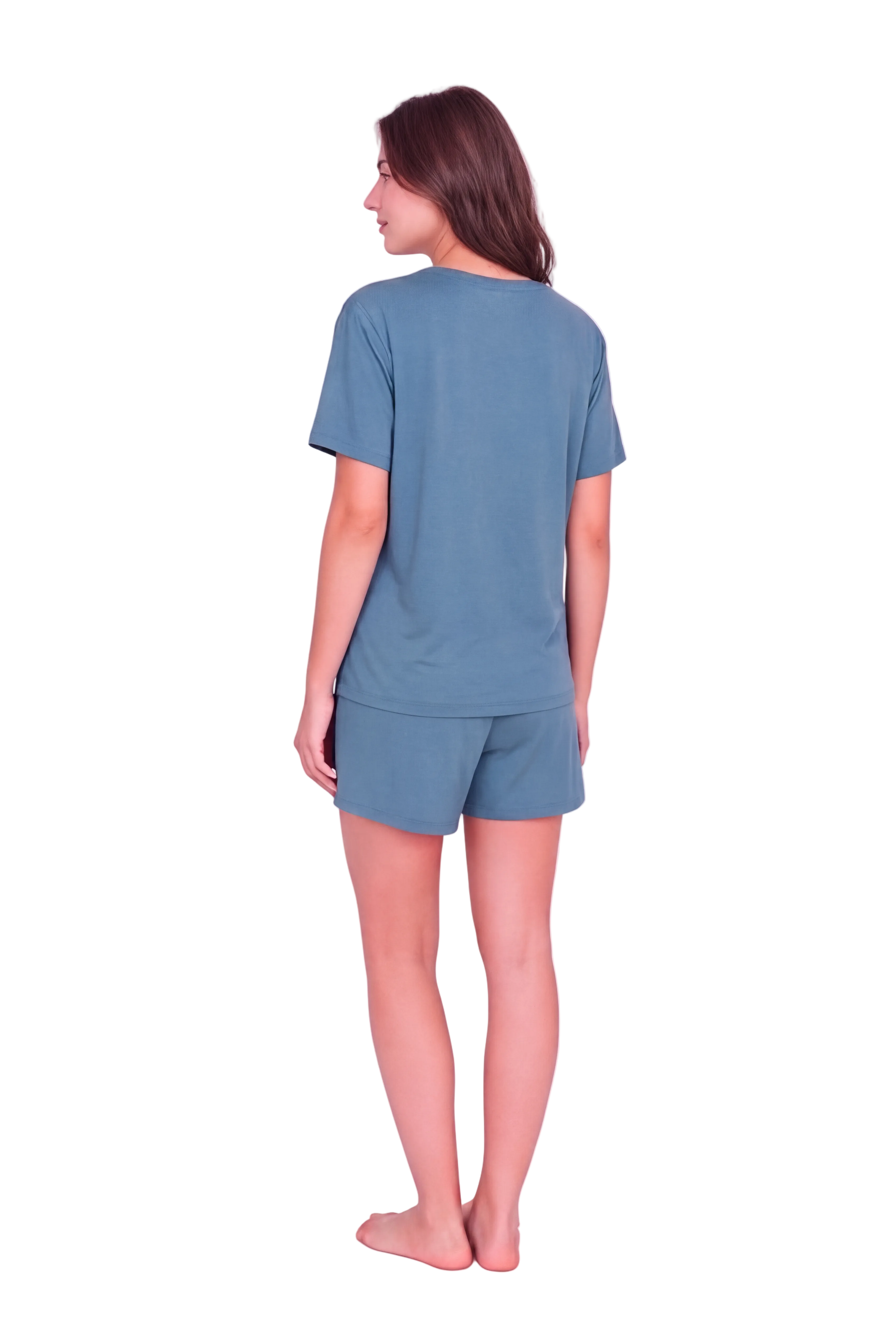 A woman stands barefoot against a light pink studio background, viewed from the back, wearing a matching dusty blue short-sleeve t-shirt and shorts set.